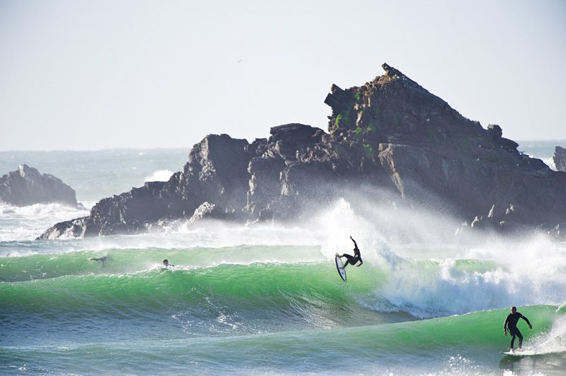 A surfer launching off the lip of a green wave below the rocks at Broken Head, Byron Bay