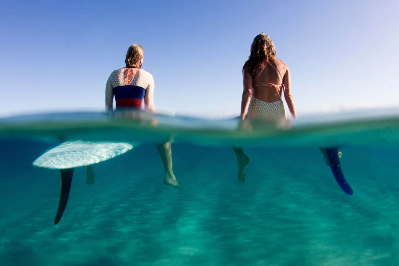 Over and under water shot of two surfers wading out through clear turquoise water with their boards